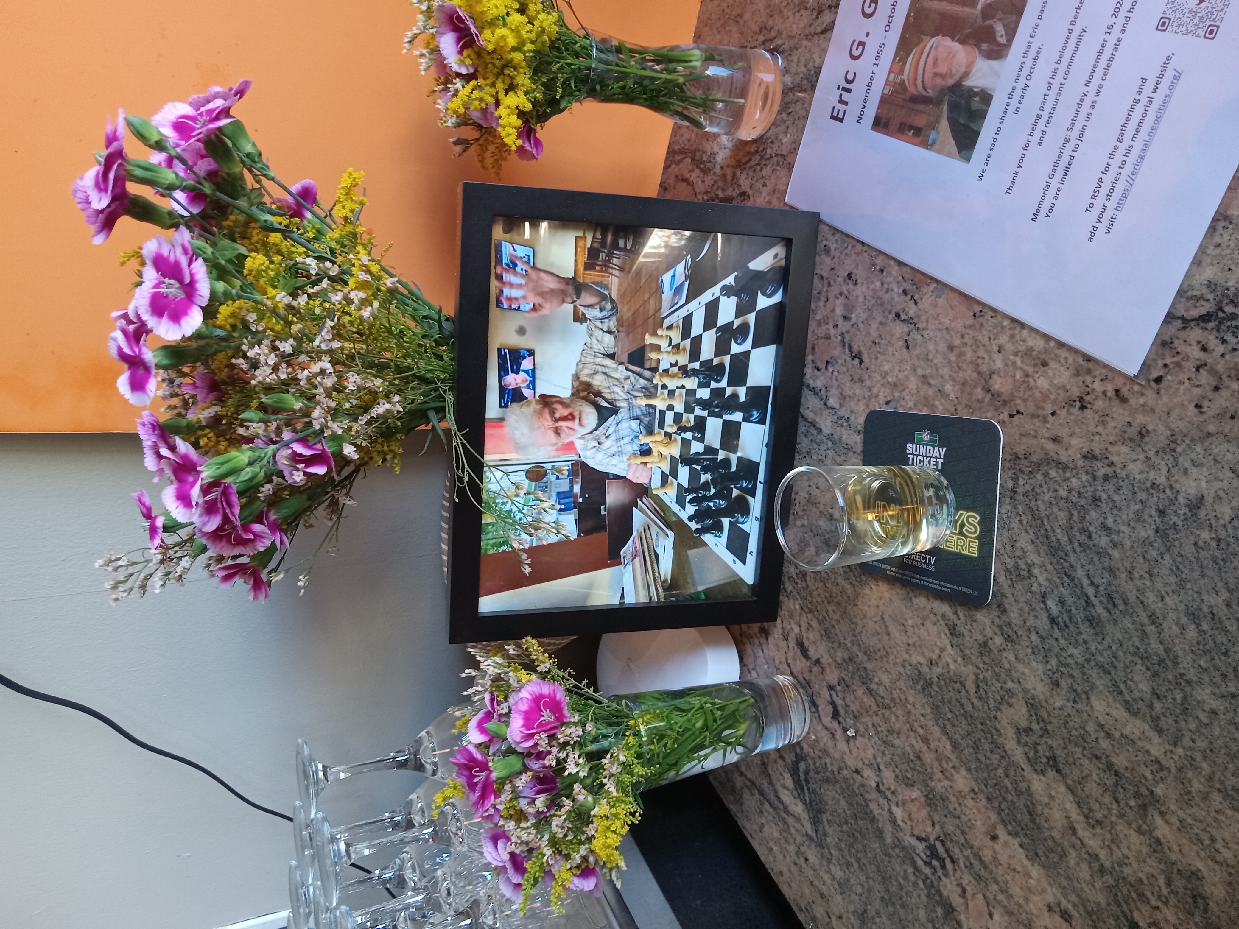 A memorial set up at Bobby G's with flowers, beer, and a photo of Eric at a chessboard